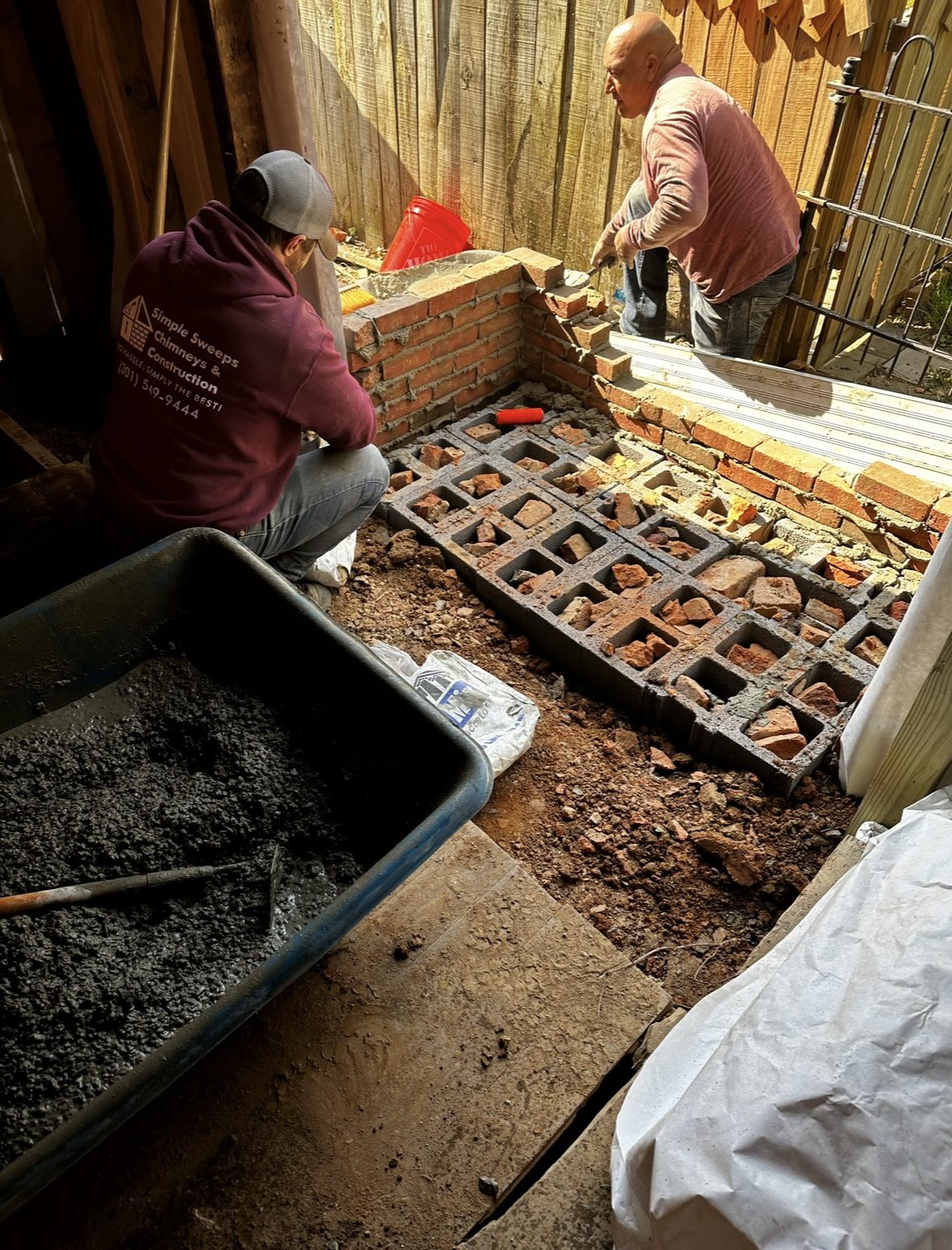 Two people working on a floor renovation with exposed wooden beams and tools.